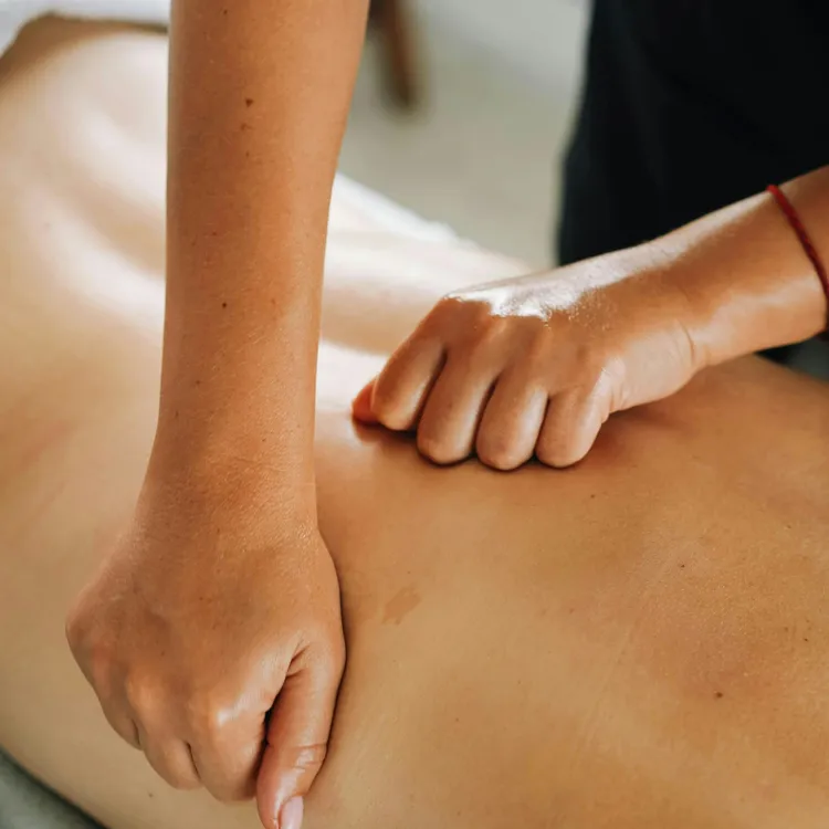 A therapist's hands working deep into the muscles of a back